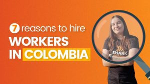 There is a Shark Helpers on the right side of the image, accompanied by a magnifying glass icon. On the left side, you'll find the title of the blog 7 Reasons to Hire Workers in Colombia.